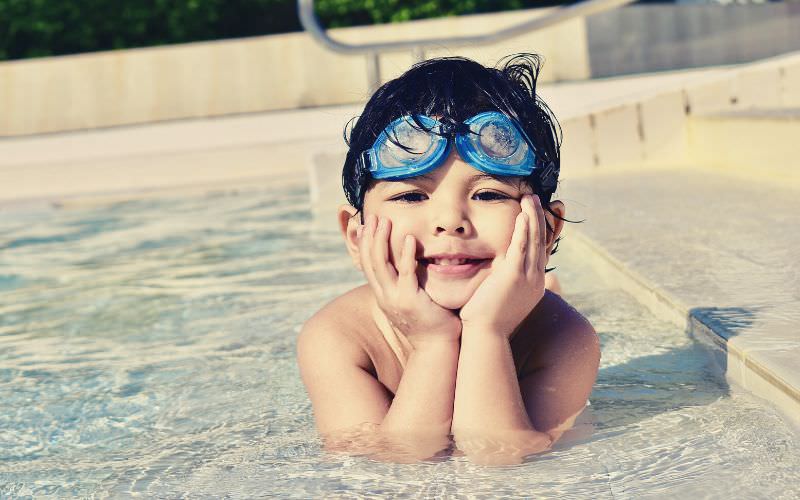 A little boy lying down in a pool's shallow end while cupping his face.
