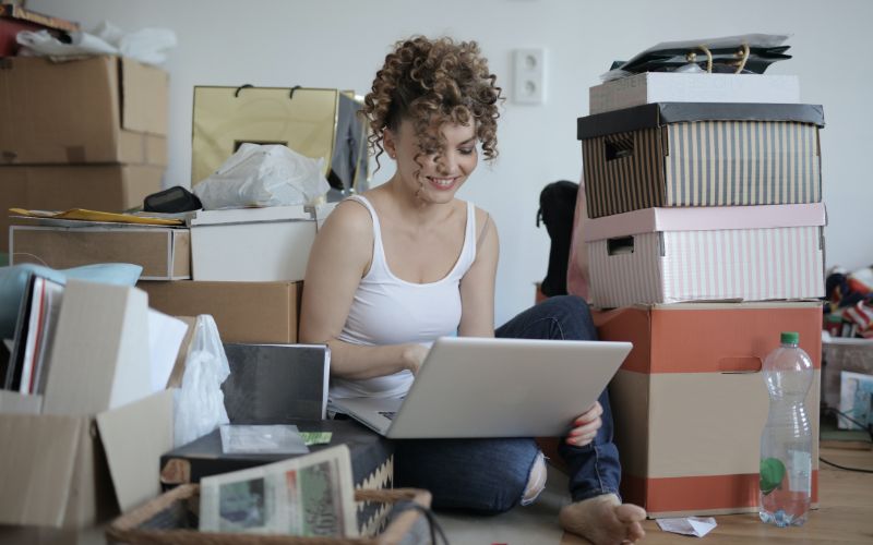Woman sitting on the floor surrounded by boxes and clutter and trying on a laptop